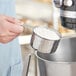 A hand using a Tablecraft stainless steel measuring cup to measure white powder.