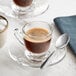 A white Acopa espresso cup on a saucer with a spoon and a bowl of sugar.