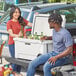 A man and woman loading a CaterGator cooler into a truck.