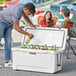 A man putting a bottle of beer into a white CaterGator outdoor cooler.