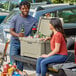 A man and woman sitting on the back of a truck with a CaterGator tan cooler.
