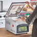 A woman using an ARY VacMaster tabletop vacuum packaging machine on a counter.
