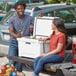 A man and woman sitting on the back of a truck with a CaterGator cooler.