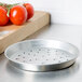 An American Metalcraft tin-plated steel pizza pan with holes next to tomatoes.