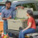 A man and woman sitting on the back of a truck with a tan CaterGator cooler.