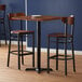 A Lancaster Table & Seating live edge bar height table with two wooden chairs.