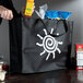 A person holding an extra-large black non-woven shopping bag with a white sun design.