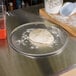 A dough ball on an American Metalcraft aluminum pizza pan on a table.