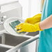 A person wearing yellow Cordova latex rubber gloves washing a dish.