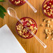 A bowl of dessert with granola and a Fineline Tiny Tasters clear plastic cocktail spoon on a table.