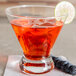 A Libbey double old fashioned glass with a drink and a lime wedge on a napkin on a table.