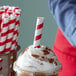 A person using an EcoChoice red and white striped paper straw to drink from a cup.