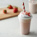 A strawberry milkshake in a plastic cup with a red and white striped EcoChoice paper straw.