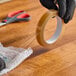 A roll of clear cellulose film tape being used to seal bubble wrap on a wooden surface.