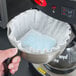 A hand using a black Urnex coffee equipment cleaner packet to clean a coffee machine.