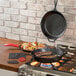 A Lodge cast iron skillet with meat cooking on a stove.