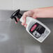 A hand holding a Weiman stainless steel cleaner and polish spray bottle over a stainless steel counter.