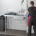 A woman washing dishes on a Regency dirty dish table in a professional kitchen.