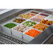 A Tablecraft brushed aluminum perforated cold well drop-in template with food in it on a counter.