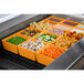 A Tablecraft orange cast aluminum bowl on a counter filled with food.