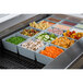 A Tablecraft gray cast aluminum bowl filled with green peas on a counter with other bowls of vegetables and food.