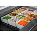 A Tablecraft black cast aluminum template with trays of food in it, including orange carrots, tomatoes, green peas, and mushrooms.