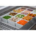 A Tablecraft white cast aluminum drop-in template with food in containers on a counter.