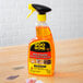 A bottle of Goo Gone Pro-Power Adhesive Remover spray gel with a yellow label on a wooden surface.