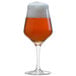 A close-up of a Stolzle stemmed beer glass full of amber beer with foam on top.