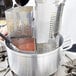 A hand uses a Vollrath stainless steel wedge inset to cook pasta over a pot.