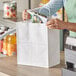 A woman opening a Duro white paper shopping bag with handles.