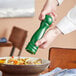 A person using an Acopa green wooden pepper mill to season a bowl of food.