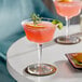 a glass of pink drink with lime and rosemary on a white table