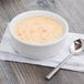 A Fiesta white china chowder bowl filled with soup with a spoon next to it.