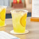 Two Choice translucent plastic cups of lemonade on a table.