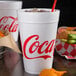 A close up of a Dart Coca-Cola foam cup filled with soda and a straw on a white background.