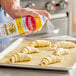 A hand spraying butter substitute on a tray of pastries.