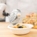 A person using a Vollrath black perforated round Spoodle to serve food.