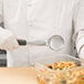 A person holding a Vollrath black perforated round Spoodle over a container of pasta.