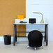 A black Safco steel round bubble wastebasket with holes in it under a desk.