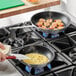 A person cooking shrimp and omelette in Choice aluminum frying pans on a stove top.