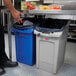 A man standing next to a grey Rubbermaid Slim Jim trash can.