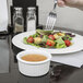 A person holding a Tuxton white fluted ramekin with a fork over a plate of salad