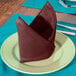 A folded burgundy Intedge cloth napkin on a plate.