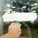 A hand holding a white Unger StripWasher with a green T-bar cleaning a window.
