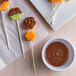 A plate of fruit skewers with chocolate on flower-shaped paper sticks.
