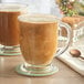 Two Acopa clear glass cafe mugs with spoons on a white surface.