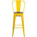 A yellow metal bar stool with a wooden seat.