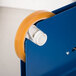 A white Shurtape cellulose film tape roll in a blue and white tape dispenser.