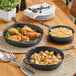 A group of Choice pre-seasoned cast iron skillets with fried chicken and potatoes on a table.